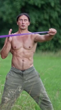 Kaslı bir birey, sakin ve sakin bir açık hava ortamında çeşitli direnç bantları gösterir.