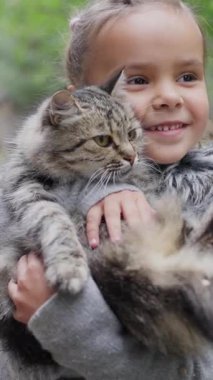 Neşeli ve kaygısız bir çocuk dışarıda güneşli güzel bir günün tadını çıkarırken tüylü bir kediyi neşeyle kucağına alır. Yavaş çekim 4k