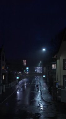 Bir bisikletçi gece yağmurda ata biner. Huzurlu ve huzurlu bir gece sokak sahnesi aşağıdaki ıslak kaldırımdaki renkli ışıkları güzel bir şekilde yansıtıyor. Yavaş çekim