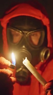 Karanlık bir yerde, gaz maskesi ve kırmızı başlıklı bir şahıs bir mum yakar, duvarlara ürkütücü gölgeler bırakır.