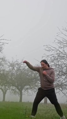 Bir dövüş sanatları uzmanı sisli bir alanda akarak dinamik hareketleri ve eğitimdeki hassasiyeti gösterir.