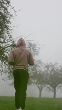 Bir adam sisli bir parkta sürekli koşuyor, sakin bir atmosfer yaratıyor ve manzaralı bir doğa sahnesi yaratıyor.