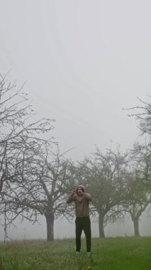 Bir insan enerjiyle sisli bir meyve bahçesine atlıyor, olağanüstü bir atletizm ve zarafet sergiliyor.