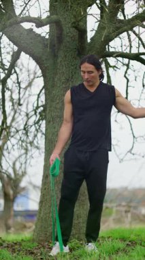 Kararlı ve odaklanmış bir sporcu direnç bantları kullanarak bir ağaca karşı esneme egzersizi yapıyor.