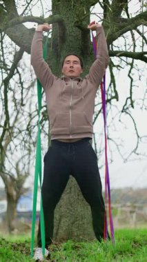Parkta egzersiz yapan bir adam, direniş bantlarını kullanarak etkili bir şekilde güç eğitimine katılıyor. Daha Sağlıklı Olmak İçin Direnç Bantlarıyla Açık Hava Fitness Gücü Eğitim Seanslarına katılıyoruz. Yüksek kalite 4k