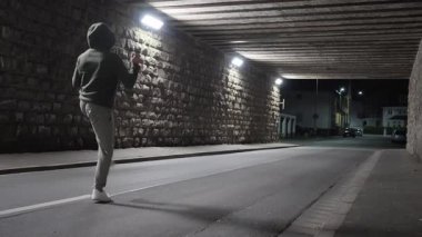 Spor giyimli bir dövüş sanatları ustası gece vakti sokak geçidi tünelinde havayı yumruklayarak dövüş kickboks egzersizi yapar. Sağlıklı erkek atlet açık havada aktif yaşam tarzı spor antrenmanlarını sever. Yavaş çekim