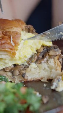 Lezzetli bir yumurta ve mantarlı kruvasan sandviçin lezzetli yakın çekimi. Lezzetli bir yemek için yumurta, mantar ve taze yeşilliklerle dolu kruvasan sandviçi. 4k