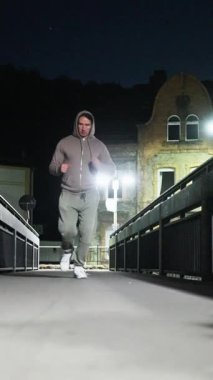 Kararlı bir koşucu gece bir köprü boyunca koşar, sokak lambalarıyla aydınlatılır, fitness ve sükuneti kucaklar..