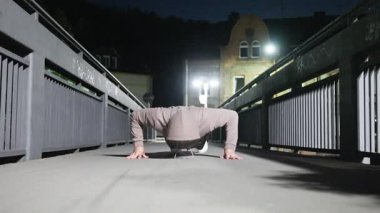 Bir insan gece vakti loş bir köprüde şınav çeker, zindelik ve kararlılık gösterir..