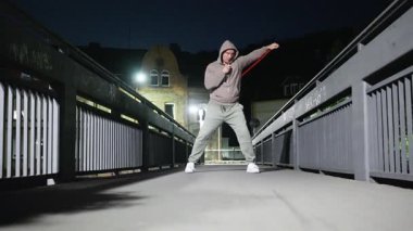 Genç bir adam geceleri köprüde dövüş sanatları pratiği yapıyor. Gücünü ve yoğun dikkatini gösteriyor.