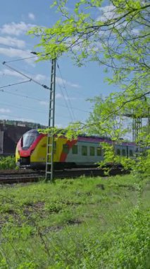 Şık ve modern bir tren, yemyeşil ve parlak mavi gökyüzüyle dolu çarpıcı bir arazide pürüzsüzce süzülüyor.