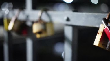Parlak renkli asma kilitlerden oluşan canlı bir koleksiyon dayanıklı bir metal korkulukta asılıydı. Geceleri güzelce aydınlatılıyordu.
