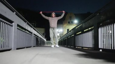 Tutkulu bir fitness meraklısı gece vakti bir köprüde direniş bantlarıyla yoğun bir antrenman yapıyor.