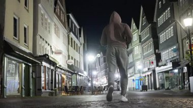 Almanya 'da tarihi binalar ve hafif ışıklandırmalarla dolu büyüleyici bir kaldırım taşı caddesinin huzurlu gece manzarası boyunca koşan bir insan. yavaş çekim