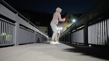 Bir insan, dayanıklılığını ve uygunluğunu vurgulamak için geceleri köprüde direnç bandı egzersizleri yapıyor. Yüksek kalite 4k görüntü