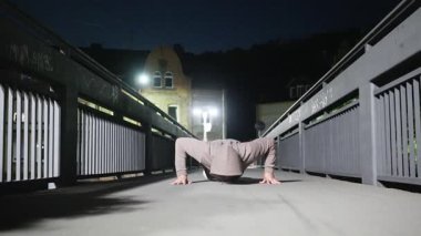 Bir insan gece vakti loş bir köprüde şınav çeker, zindelik ve kararlılık gösterir. Yüksek kalite 4k görüntü