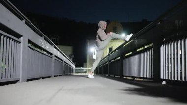 Gece vakti köprüde gerinen bir insan, güzel bir şekilde zindelik, denge ve kentsel yaşam tarzını gösteriyor.