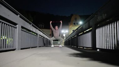 Bir atletin direniş bandı kullanırken gücünü gösterdiği dinamik ve enerjik bir gece sahnesi.