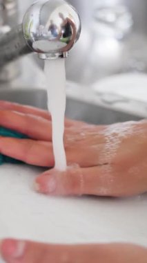 Sürekli akan suyun altında, sabunla ve süngerle güçlü bir şekilde yıkanan ellerin yakın görüntüsü.