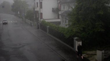 Yağmurlu bir günü tasvir eden bir sahne. Yalnız bir şahıs sisle kaplı şehir mimarisinde yürüyor.