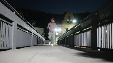 Geceleri köprüde koşan bir insan, açıkça zindelik seviyesini ve çevrendeki canlı şehir yaşamını gösteriyor.