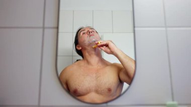 Bir adam banyoda tıraş oluyor, kişisel bakım ve kişisel bakım rutinlerinin önemini gösteriyor.