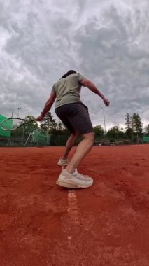 Bir tenis oyuncusu, fırtınalı bulutlarla dolu bir sahada, atletizm ve beceri gösterisi yaparken yakalanır. Ağır çekim. Yüksek kalite 4k görüntü