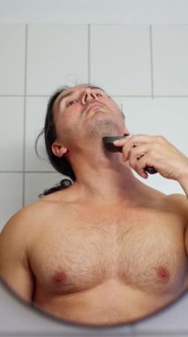 Bir adam aynanın önünde sakalını tımar ediyor, günlük bakımını yapıyor ve kişisel sağlığını destekliyor. Yüksek kalite 4k görüntü