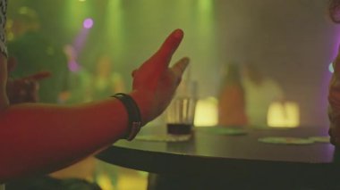 Dinamik gece hayatı, ellerin bardakları tokuşturması ve canlı içeceklerin tadını çıkarmasıyla hareketli ortamı gözler önüne seriyor.
