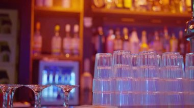 Şık ve modaya uygun bir bar sahnesi. Renkli içki şişelerinin yanında parlak ışık altında istiflenmiş bardaklar.