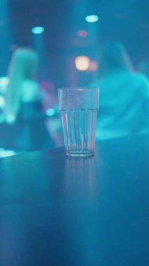 Temiz bir içki bardağı renkli ışıklandırması ve bulanık arkaplanı olan modaya uygun bir barda oturur ve canlı bir hava yaratır.