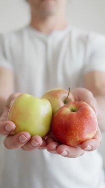 Çıtır beyaz bir gömlek giyen bir insan, üç canlı ve taze elma tutuyor, sağlıklı seçenekleri vurguluyor.