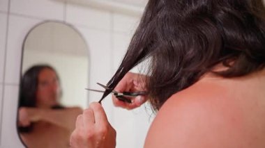 Evde aynanın önünde uzun saçlarını kesen bir adam, DIY tımar ve kişisel bakım sergiliyor..