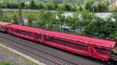Açık mavi gökyüzünün altında, yemyeşil yemyeşil güzel çerçevelenmiş, rayların üzerinde canlı bir kırmızı tren vagonu dizili.