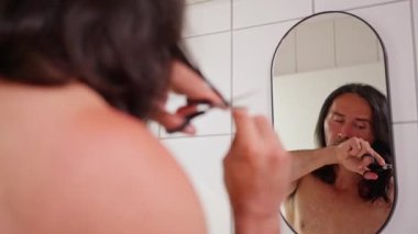 Evde, aynanın önünde uzun saçlarını kesen bir insan DIY tımarı ve kendine bakımı sergiliyor. Kolay ve Şık Sonuçlar İçin Banyo 'da Saç Tıraşı Doğru Yapıldı. 4k görüntü