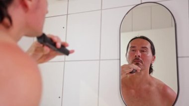 Bir adam duşta tıraş oluyor, özen gösteriyor ve modern tımar alışkanlıkları sergiliyor.