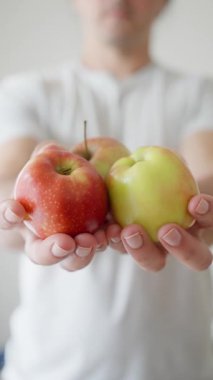 Bir adam parlak kapalı bir ortamda kırmızı ve yeşil elmalar sunar. Tazelik ve tercih sunar..
