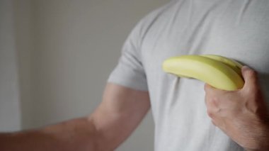 Güçlü vejetaryen, vegan adam, kaslarını gösteriyor. Sıcak ve davetkar bir ortamda, bir insan canlı olgun muzlar sunar, ilgi ve haz çeker. Yüksek kalite 4k görüntü