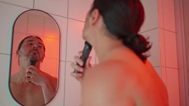 Bir beyefendi güzel, modern bir banyoda tıraş oluyor. Çevrede ışıklandırma ve kişisel bakım var.