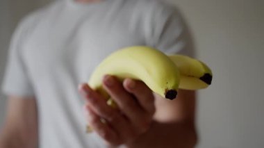 Neşeli bir insan olgun, taze sarı muzları nazikçe bulanık bir arka plan manzarasının önünde tutuyor.