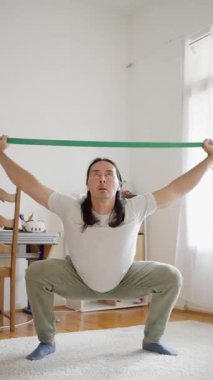 Bir insan evdeki direnç bantlarıyla çalışıyor, hem form seviyesini hem de esnekliği arttırmayı hedefliyor.