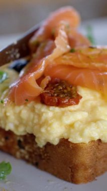Lezzetli tost, bol bol çırpılmış yumurta, tütsülenmiş somon ve taze otlarla kaplıdır. Yüksek kalite 4k görüntü