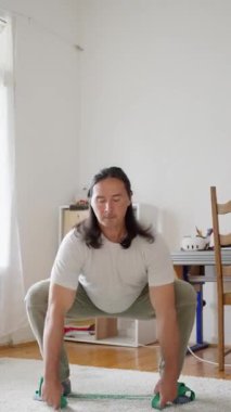 Dikey video. Bir adam direnç bandı egzersizleri yapıyor. İçerideki güç antrenmanlarını geliştirmek için. Yüksek kalite 4k görüntü