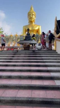 Pattaya. Tayland. 21 yaşında. 02 numara. 2023. Renkli çiçekler ve çeşitli ziyaretçilerle çevrili büyük altın bir Buda 'nın olduğu sakin bir tapınağı ziyaret edin. Dikey video