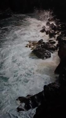 Okyanusun güçlü dalgalarının bu nefes kesici deniz manzarasında engebeli kayalara çarpmasına tanık olun. Dikey video. Yüksek kalite 4k görüntü
