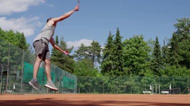 Aydınlık bir kortta, yemyeşil ortamda tenis oynayan yetenekli bir atlet profesyonel hareketler sergiliyor..