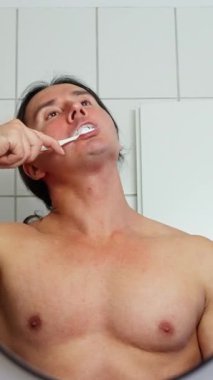 Bir adam banyoda duruyor, dişlerini fırçalıyor ve kişisel hijyene ve günlük rutinine odaklanıyor. Yüksek kalite 4k görüntü