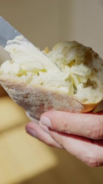 Parlak, davetkar bir şekilde taze bir ekmek parçasına nazikçe yayılan bir elin detaylı bir yakın çekimi.