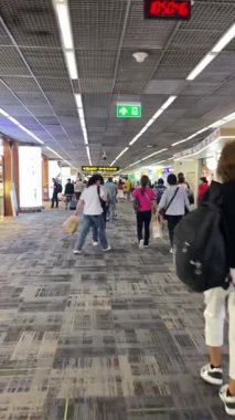 Gezginlerle, çeşitli işaretlerle ve sürekli hareketlerle dolu yoğun bir havaalanı terminali. Çok sayıda yolcunun çağdaş bir terminalde gezindiği canlı ve hareketli bir havaalanı sahnesi