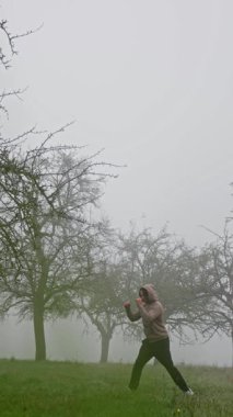 Sisli bir meyve bahçesinin ortasında hareketli ve enerjik hareketler yapan aktif ve sağlıklı bir yaşam tarzı sergileyen bir insan.
